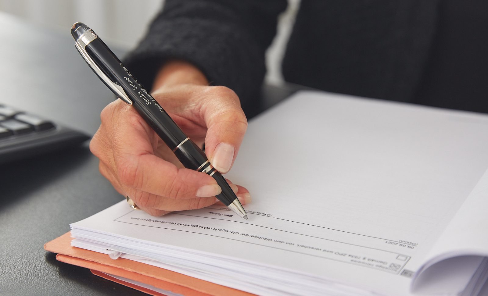 Hand mit Füller unterschreibt einen Vertrag auf dem Schreibtisch der Kanzlei
